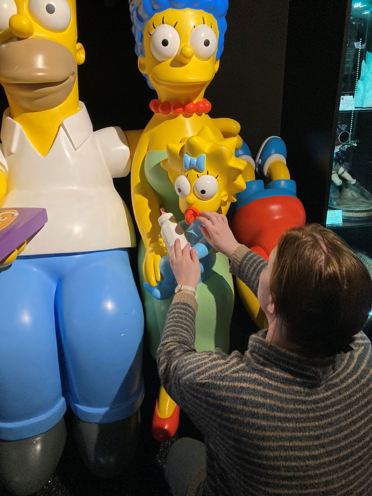 Žena čupí pri plastovom súsoší rodiny Simpsonovcov a hmatom si prezerá Maggie.