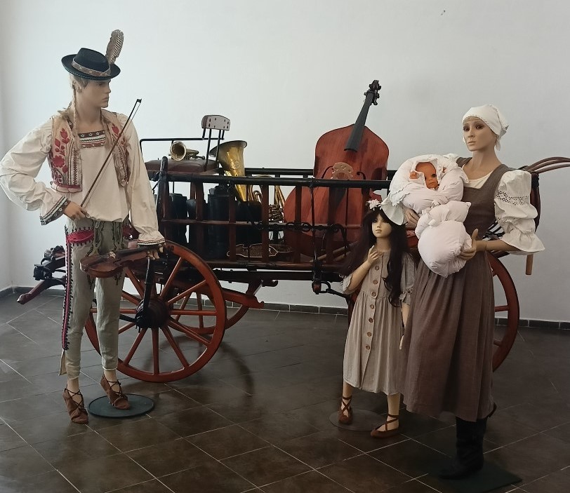 Na fotografii je voz, v ktorom sú rôzne hudobné nástroje. Pred kočom sú umiestnené figuríny - huslista s nástrojom v ruke, mladá matka s dieťaťom v náručí a ďalšie malé dievčatko.