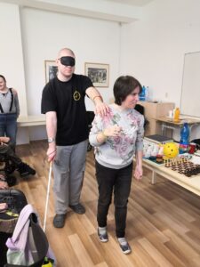 Ďalší dvaja klienti si skúšajú priestorovú orientáciu s orientačnou palicou. Žena je menšia a muž je vyšší. Obom sa táto činnosť veľmi páči. 