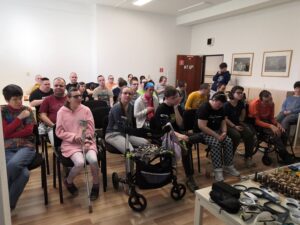 Skupina klientov zariadenia DSS ROSA sediaci vo veľkej miestnosti, ktorí sa dívajú na sociálne pracovníčky ÚNSS