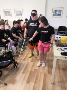 Ďalšie skúšanie ovládania orientačnou palicou s dvoma klientmi. Diváci klienti ich sledujú. 