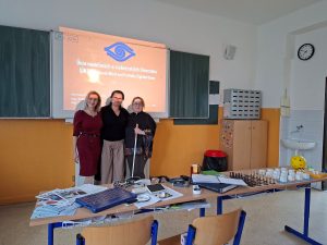 Skupinový záber pracovného tímu únie a krajského strediska v triede školy. Pred nimi je stôl, na ktorom prezentujú pomôcky pre nevidiacich. 