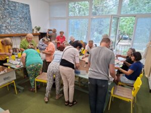 Veľká skupina ľudí pracuje na skladaní pokladničiek a balení bielych pasteliek. 