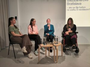 Štyri ženy sediace na stoličkách tvárou k publiku. Dušana Blašková drží v ruke mikrofón a vedie diskusiu na tému debariérizácie mesta Bratislava 
